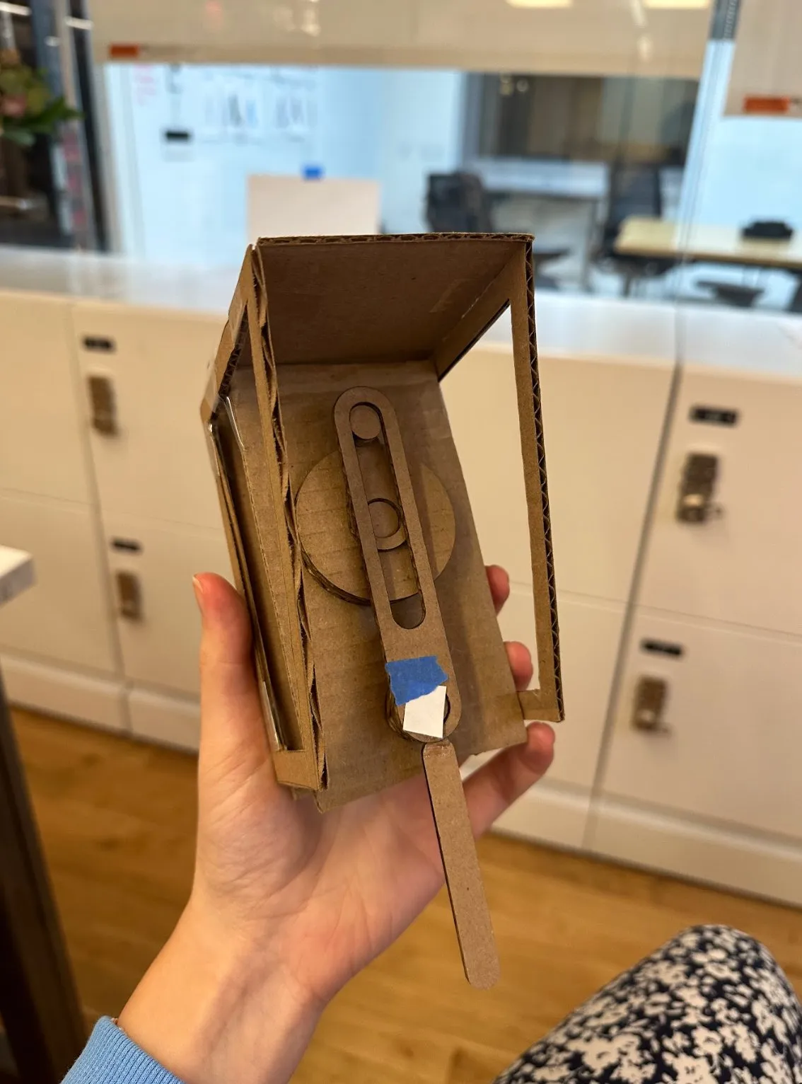 A hand holding the cardboard hollow frame prototype up in the studio, with the slot and shelf visible.
