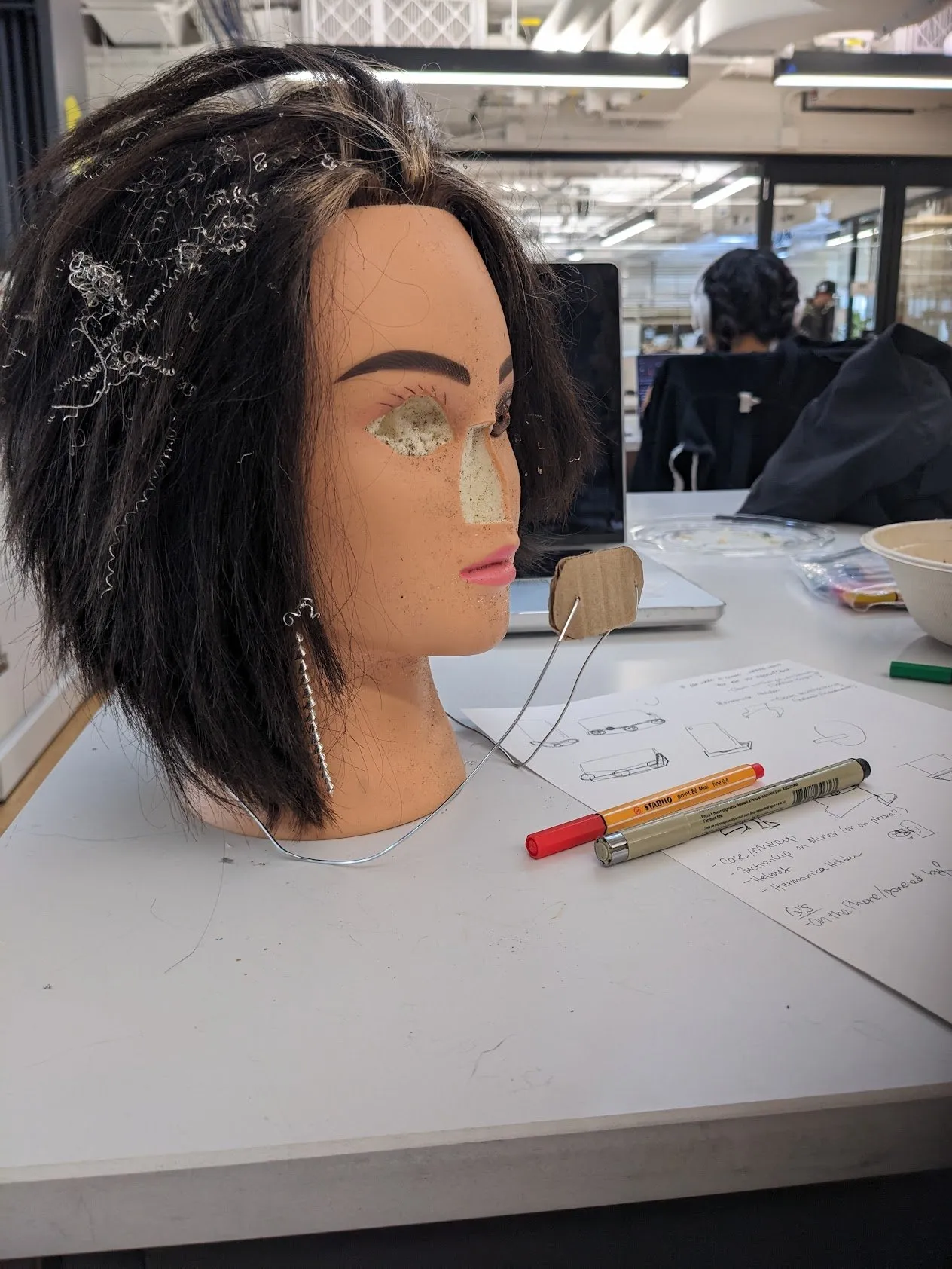 A wigged mannequin head sitting on a studio table, used as a stand-in for testing face position.