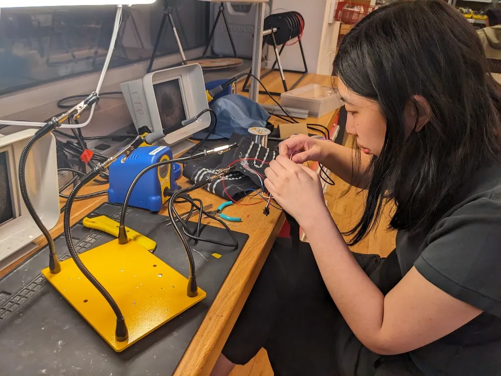 A photograph of a young Asian woman soldering wires at a workstation