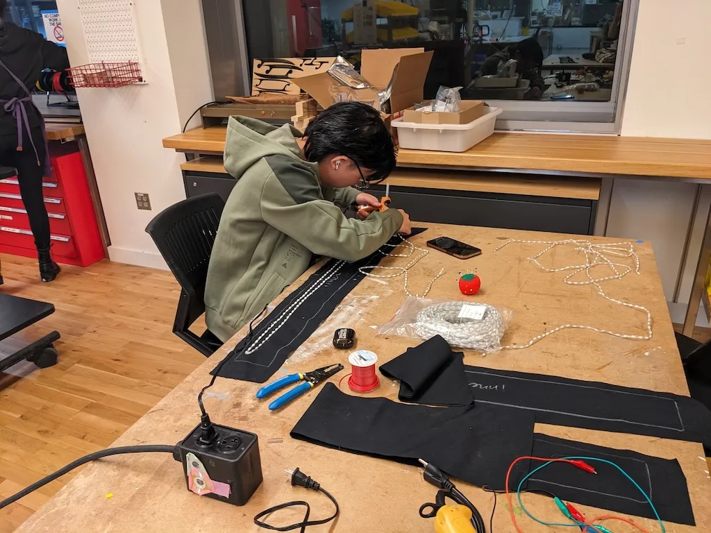 A photograph of a young Asian man hot gluing lights onto a piece of black fabric