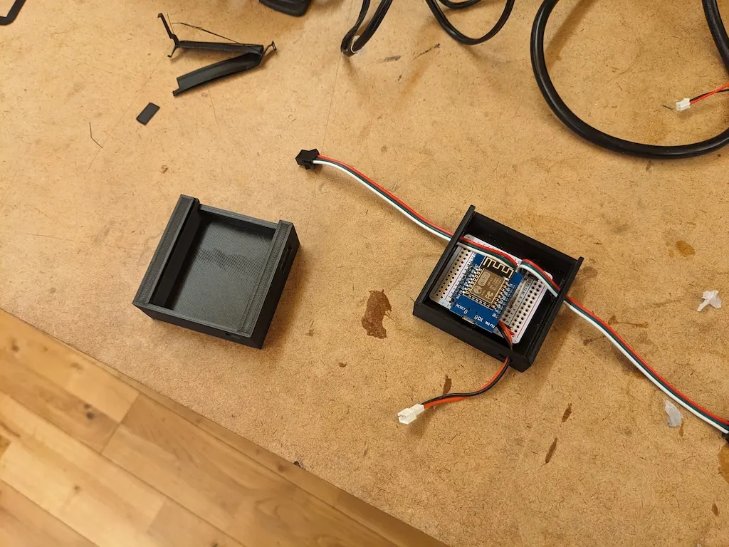 A photograph of the top of a table showing a 3D printed enclosure with a protoboard and a small circuit board inside.