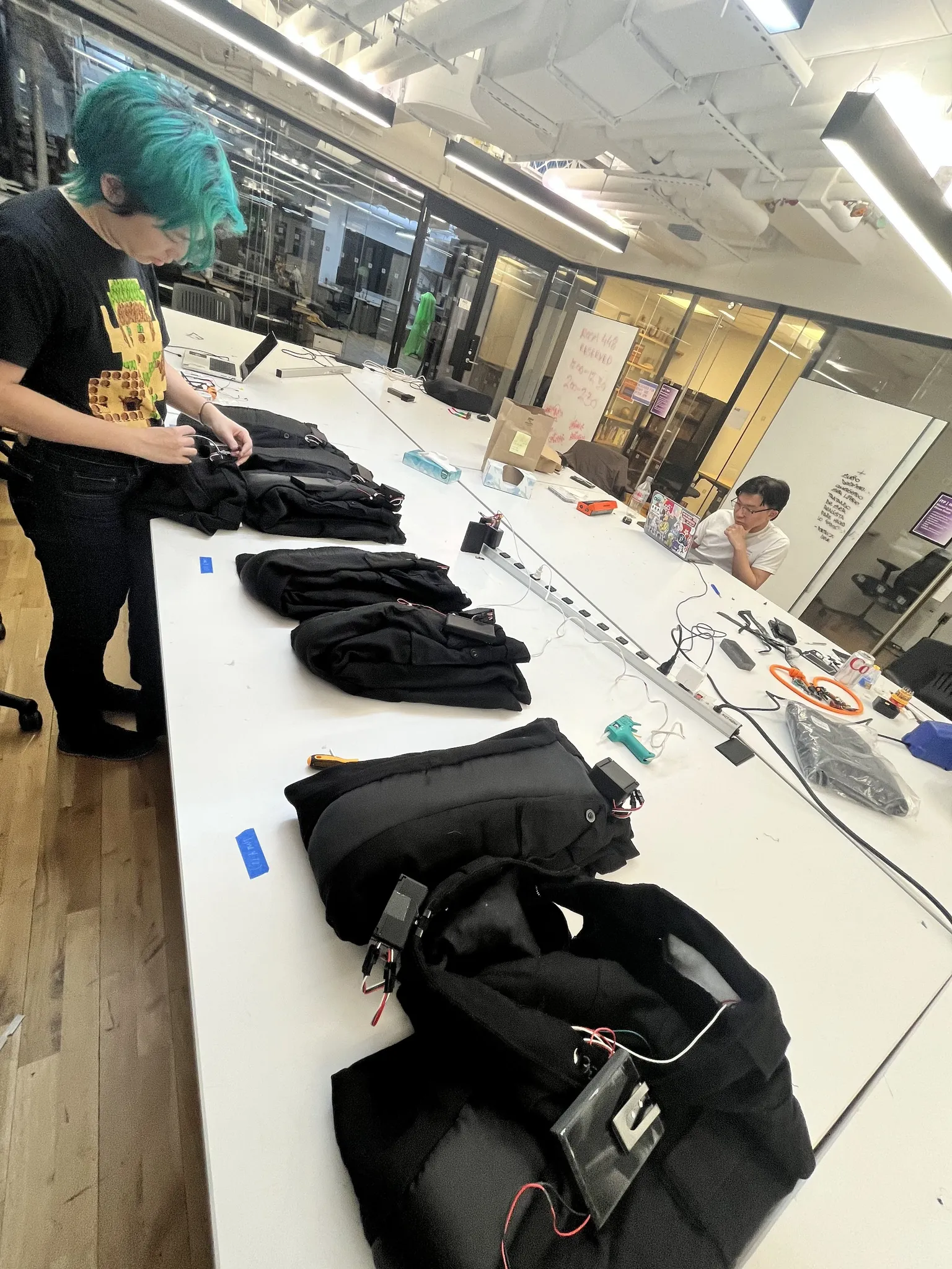 A photograph of a green haired woman adjusting some pants laying on a table