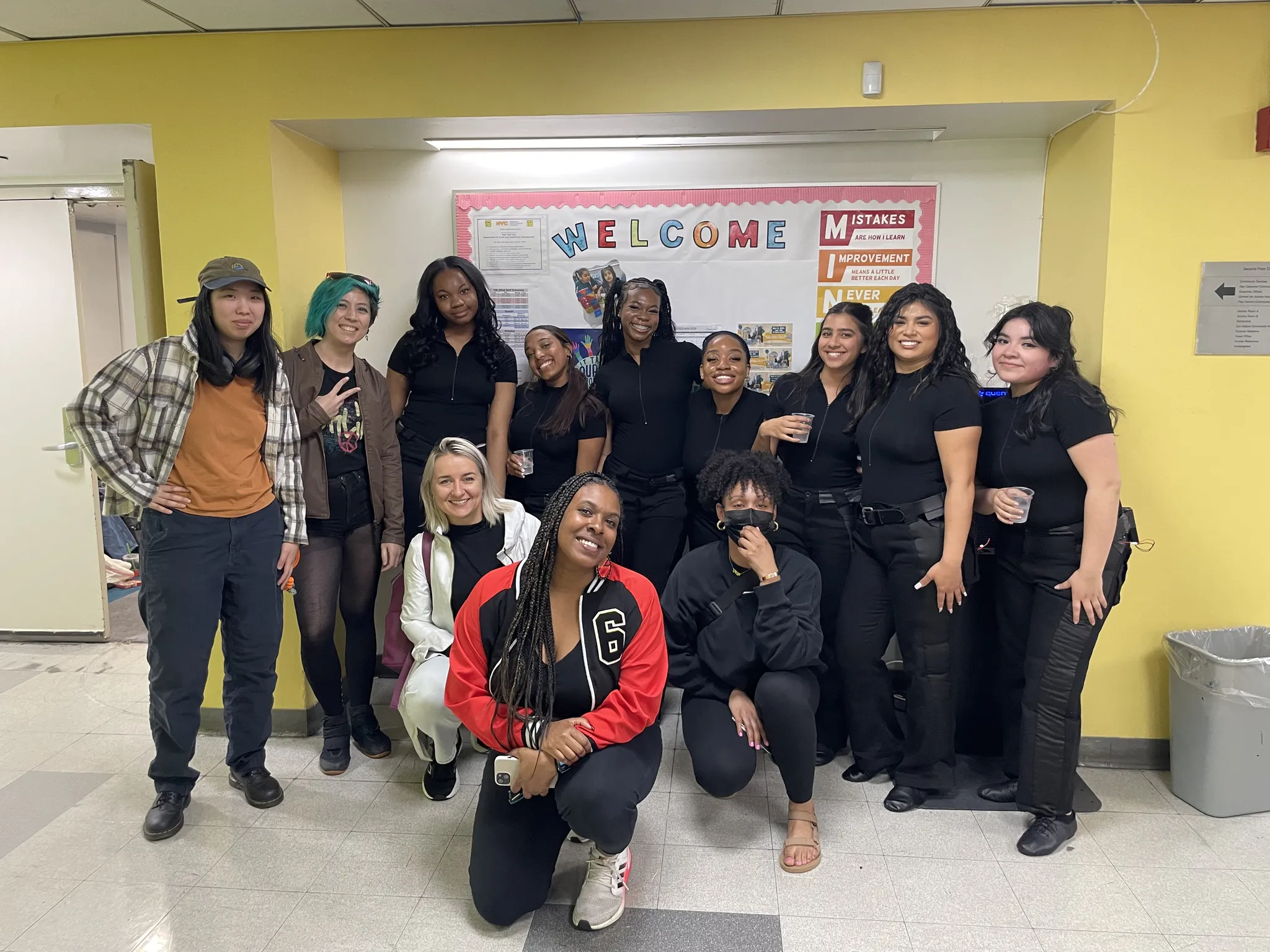 A photograph of a team of dancers and the author posing in front of a wall at a school