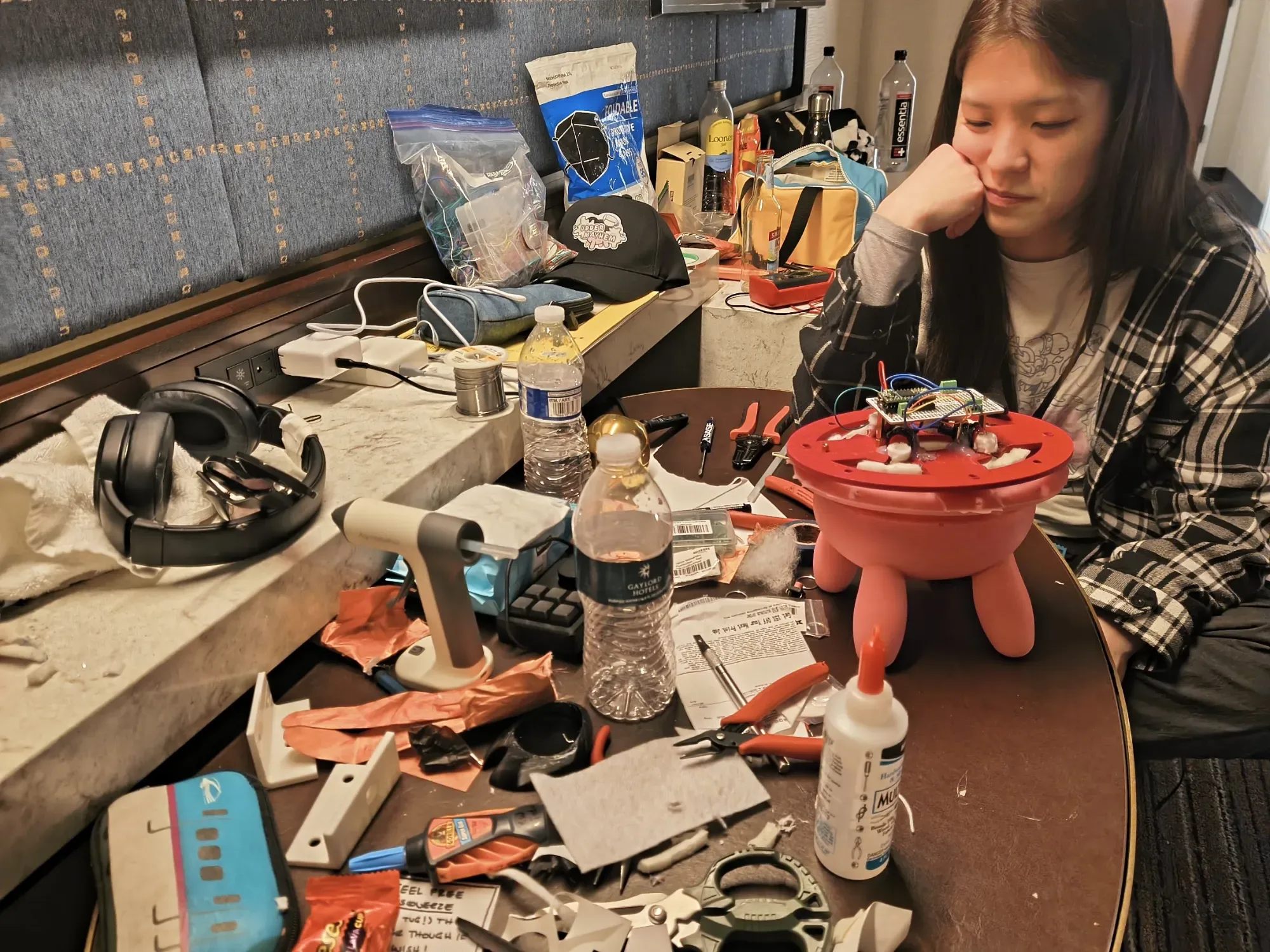 Photograph of a friend staring down the button udder on a hotel room table covered in tools