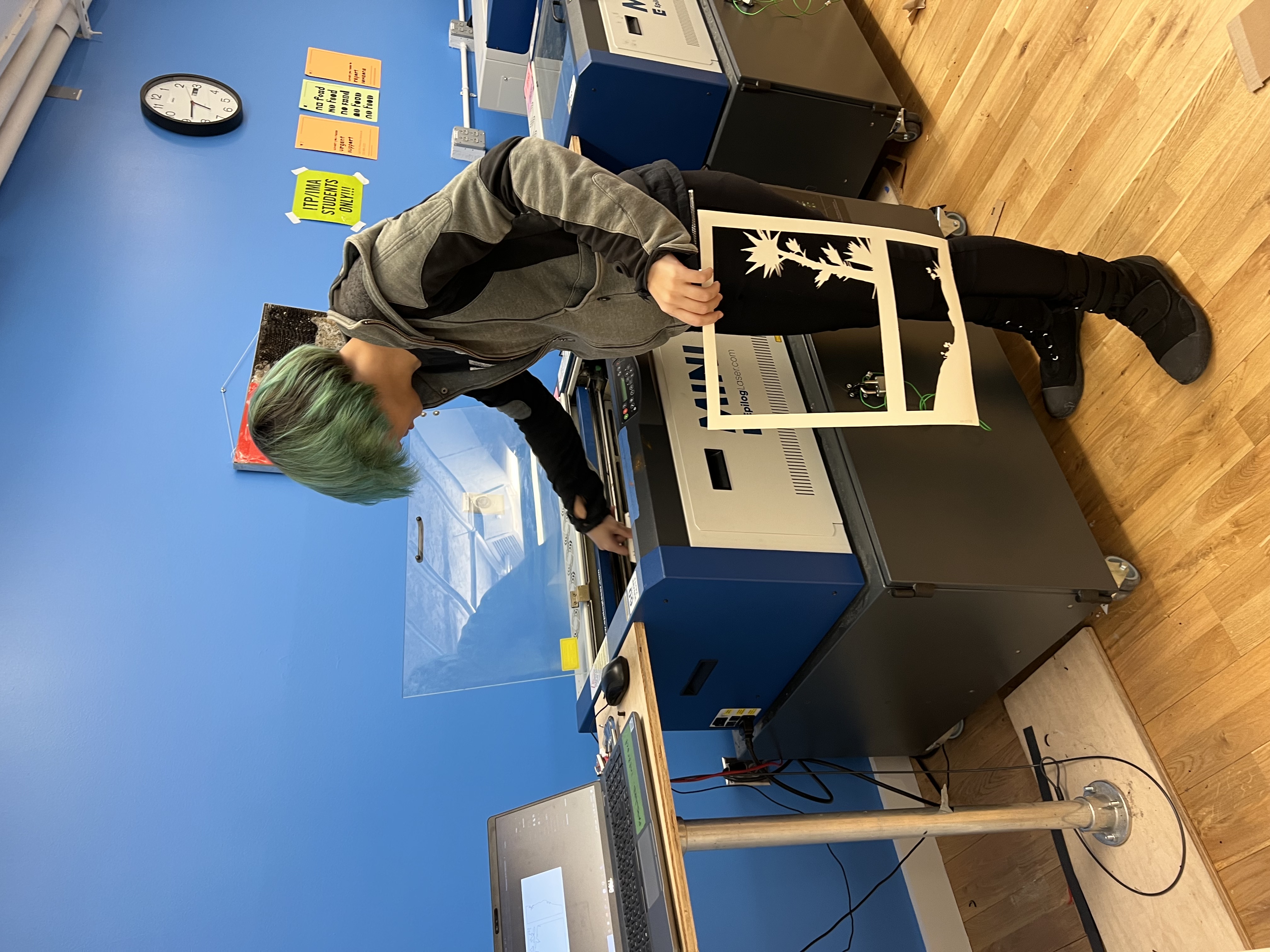 Photograph of a green haired woman waiting for the laser cutter