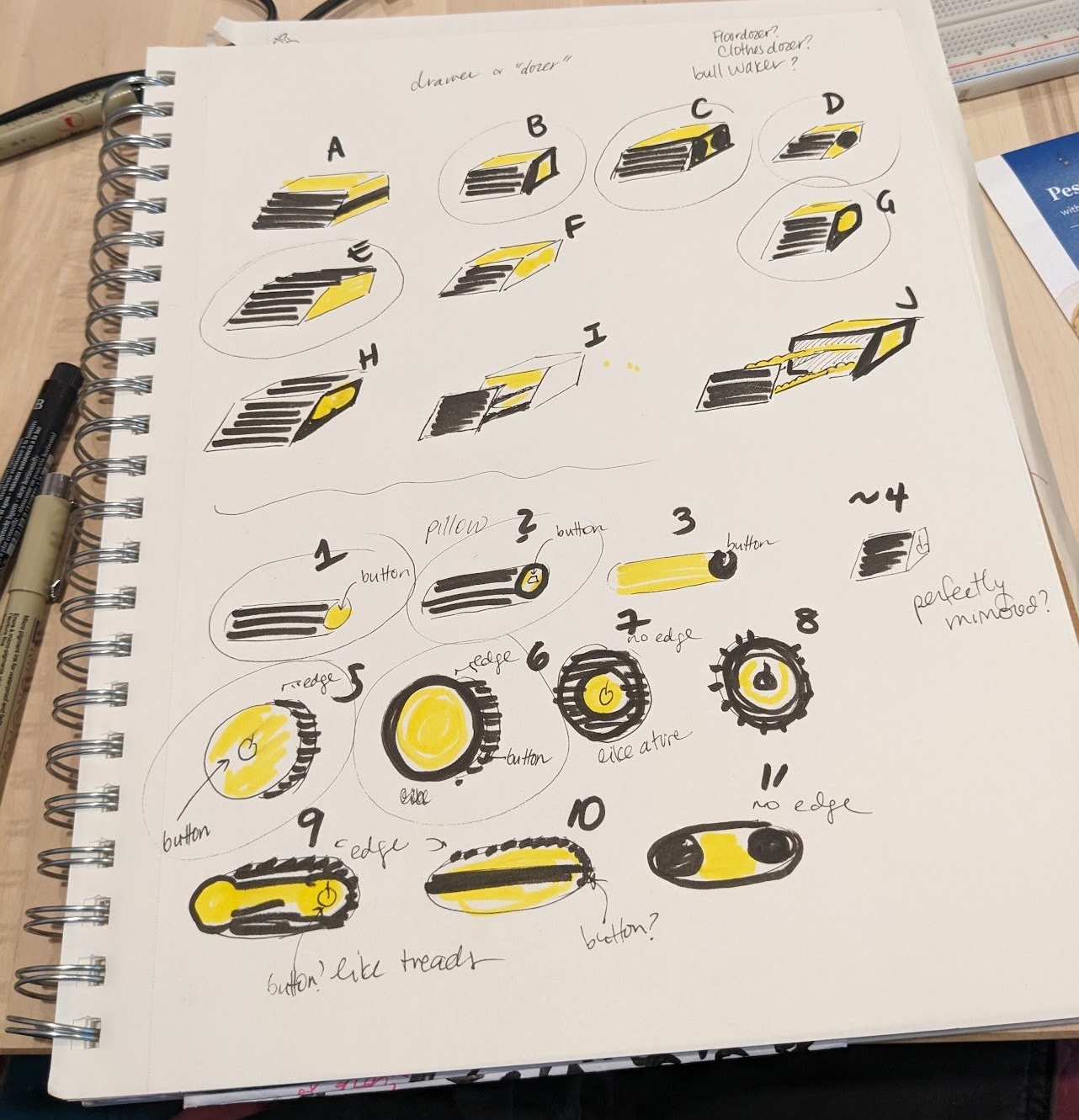 The image shows a sketchbook page filled with various hand-drawn designs and annotations. The sketches depict different shapes and features, primarily in black and yellow, labeled with letters (A to J) and numbers (1 to 10). The designs appear to focus on buttons, edges, and other functional elements, with notes such as "button," "pillow," "edge," and "no edge." There are also questions written in the margins, such as "perfectly min???" and "button? like thread?" The overall layout suggests a brainstorming session for product design or concept development.