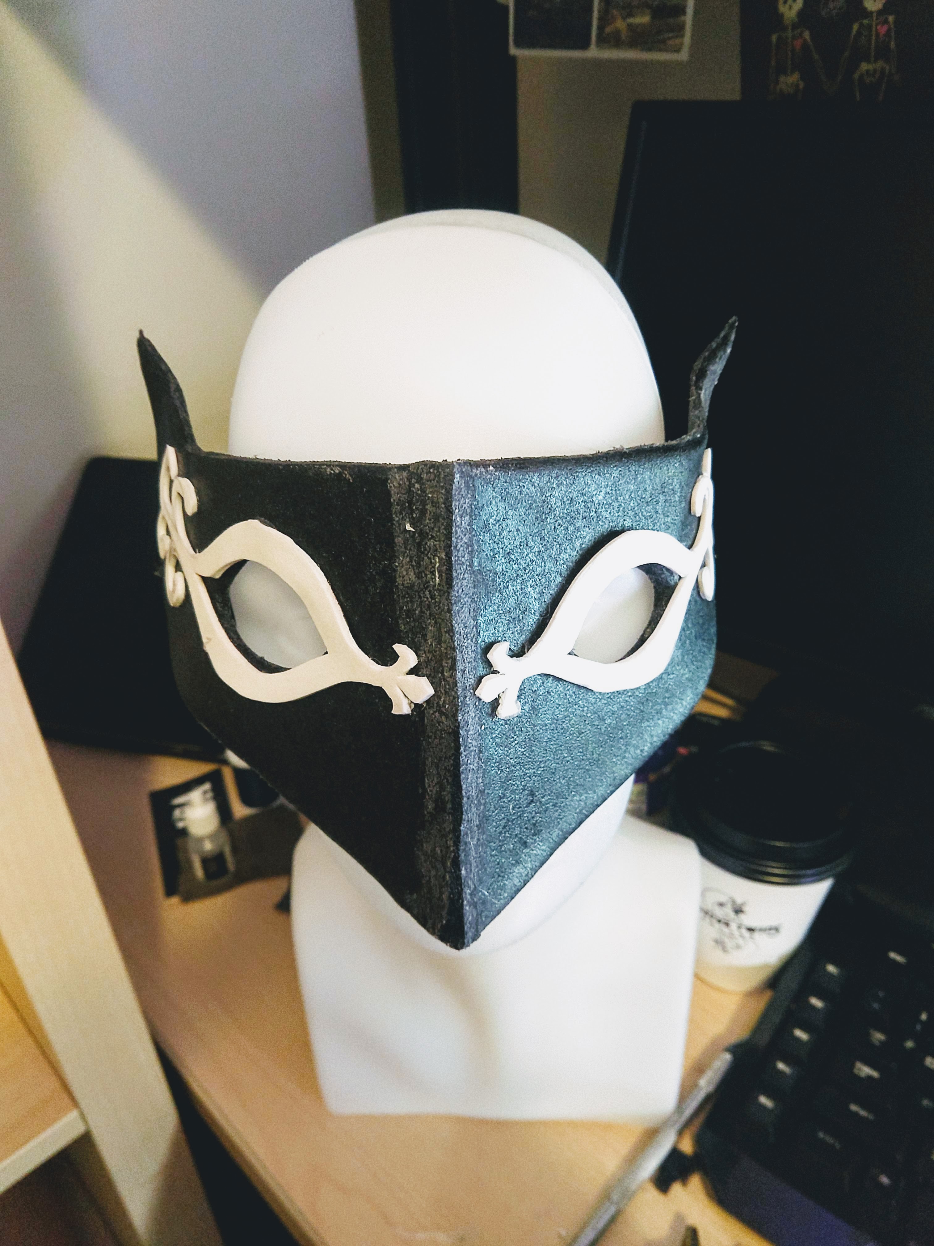 Photograph of a black mask with detailed designs around the eyes sitting on a head mannequin