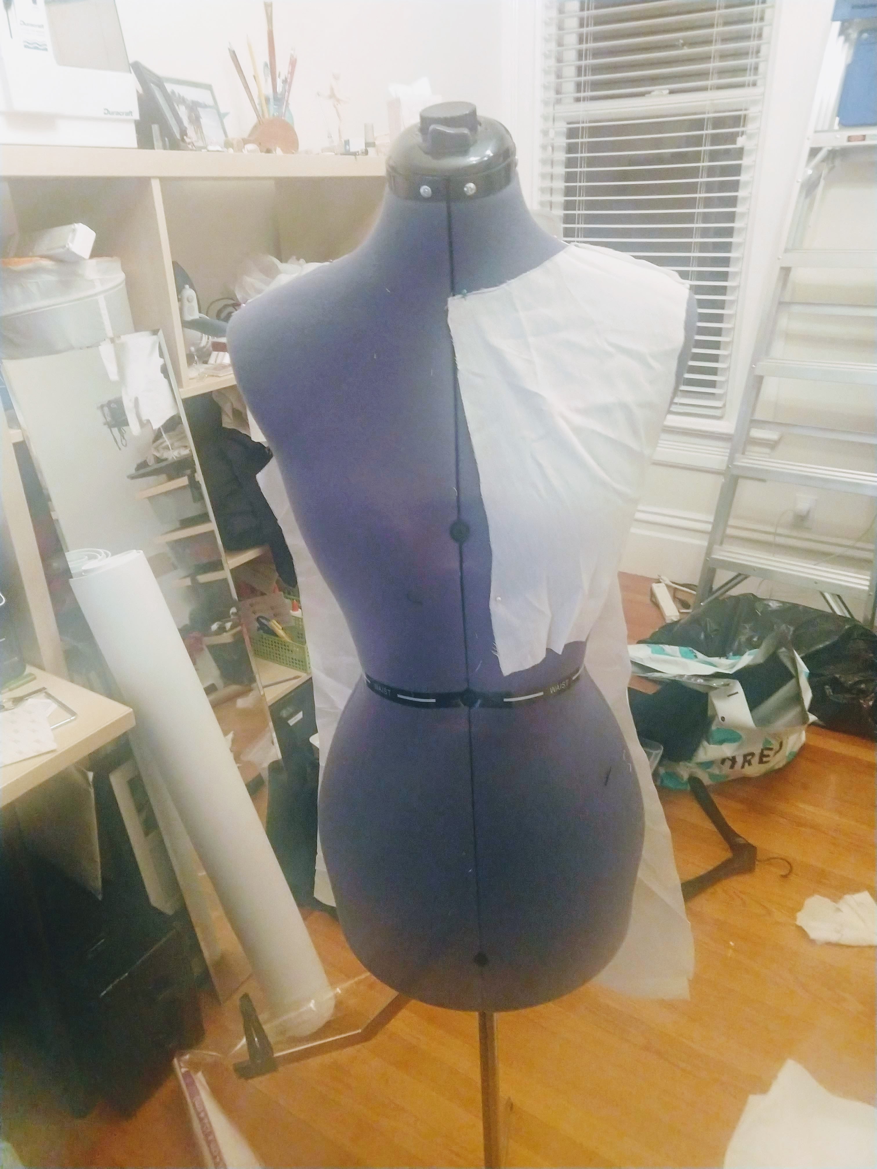 Photograph of a mannequin from the front with white muslin fabric draping off