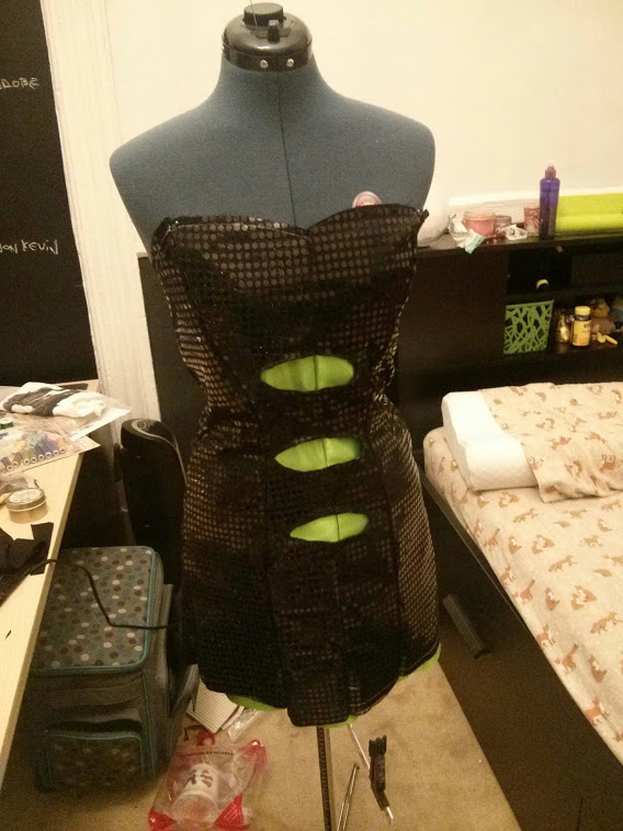 Photograph of a black sequins dress with green cutouts on a mannequin