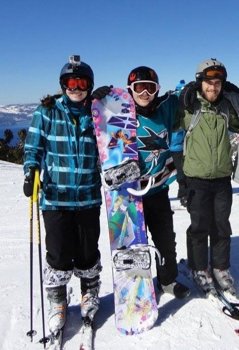 Photograph of a group of snowboarders, the one in the center holding up his Zelda and Star Wars themed snowbard